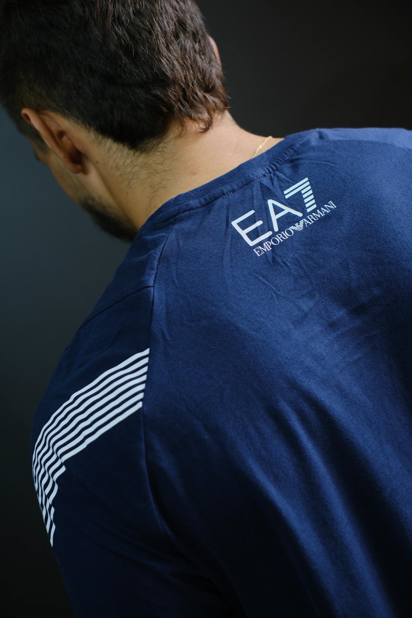Camiseta azul marino de hombre con logo y líneas blancas en los hombros, vista desde atrás