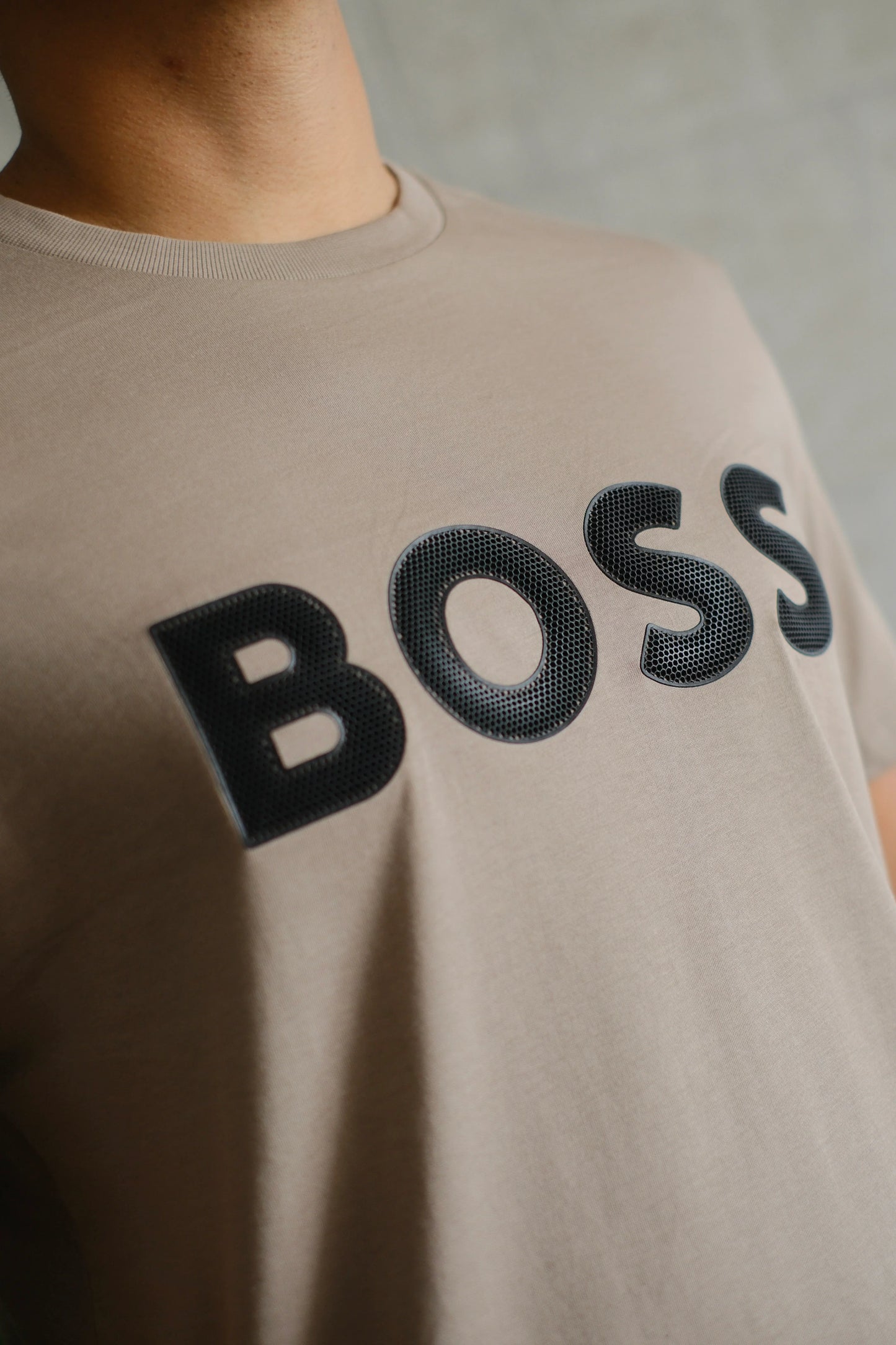 Camiseta beige con la palabra BOSS en letras negras en relieve, estilo casual moderno.