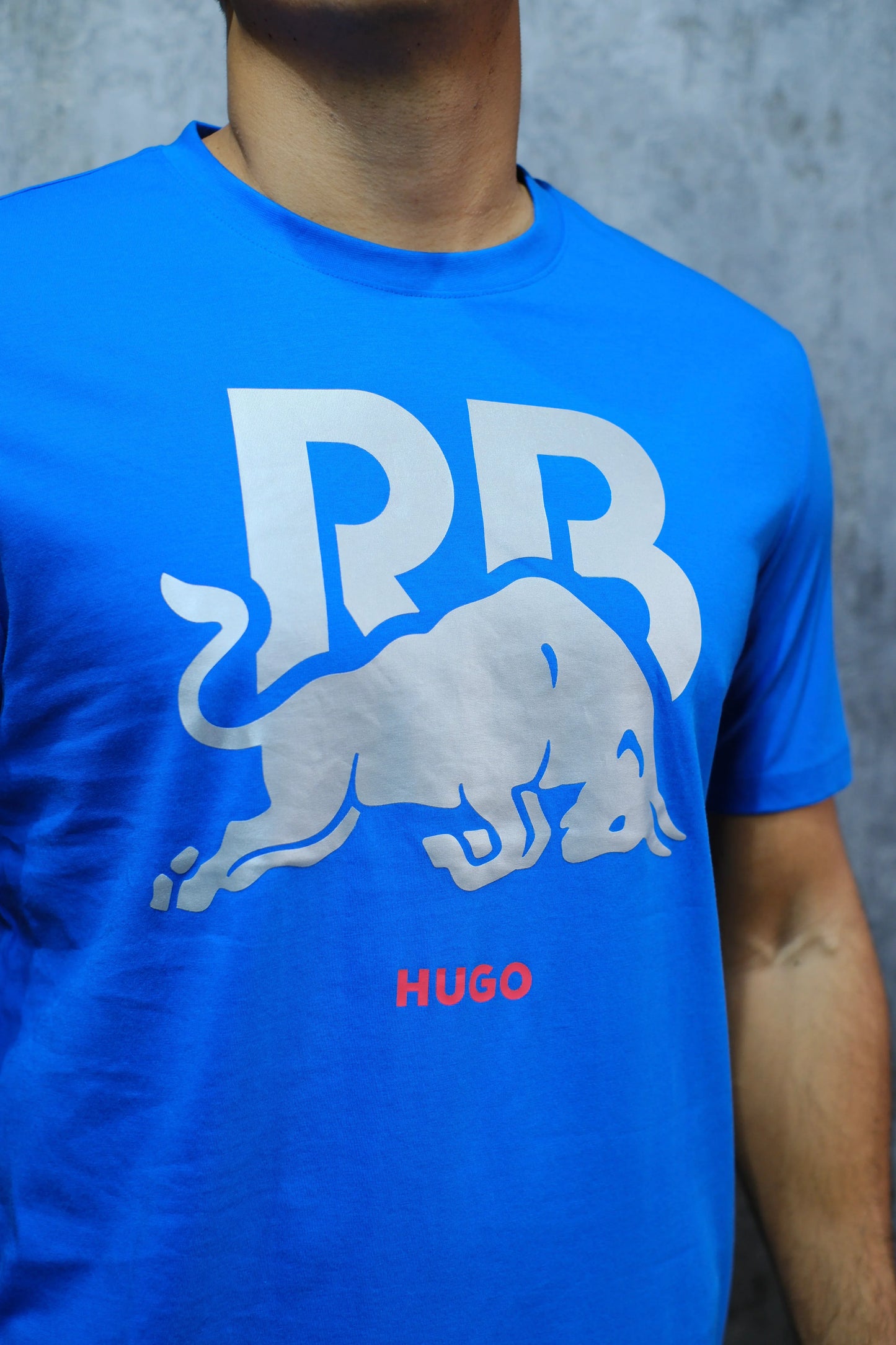 Camiseta azul para hombre con toro blanco y letras RB grandes, palabra HUGO en rojo.