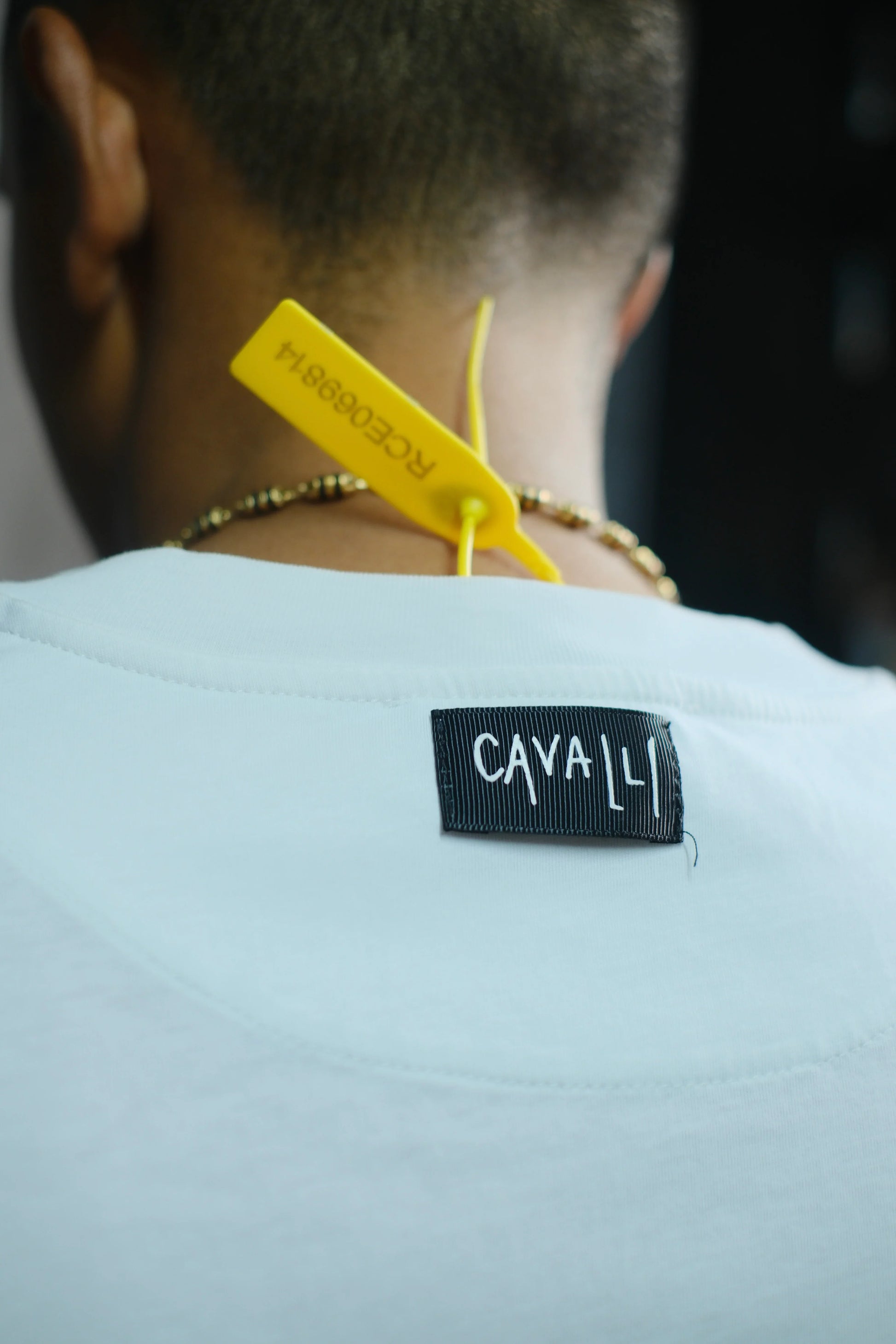 Etiqueta CAVA LI en camiseta blanca con etiqueta amarilla y collar dorado, moda urbana.