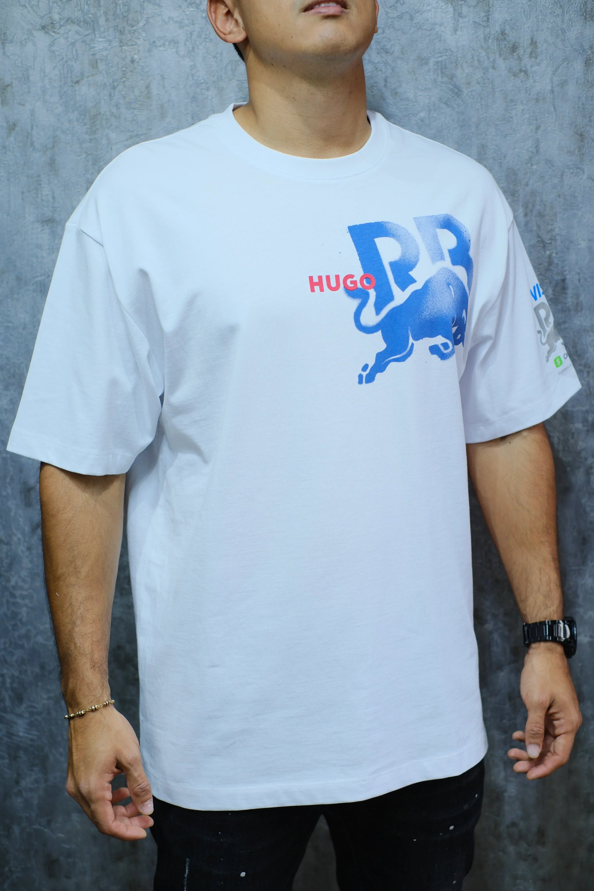 Hombre vistiendo camiseta blanca con estampado azul y rojo de toro y letras, fondo gris