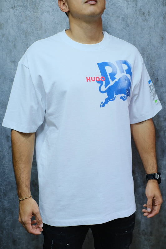 Hombre vistiendo camiseta blanca con estampado azul y rojo de toro y letras, fondo gris