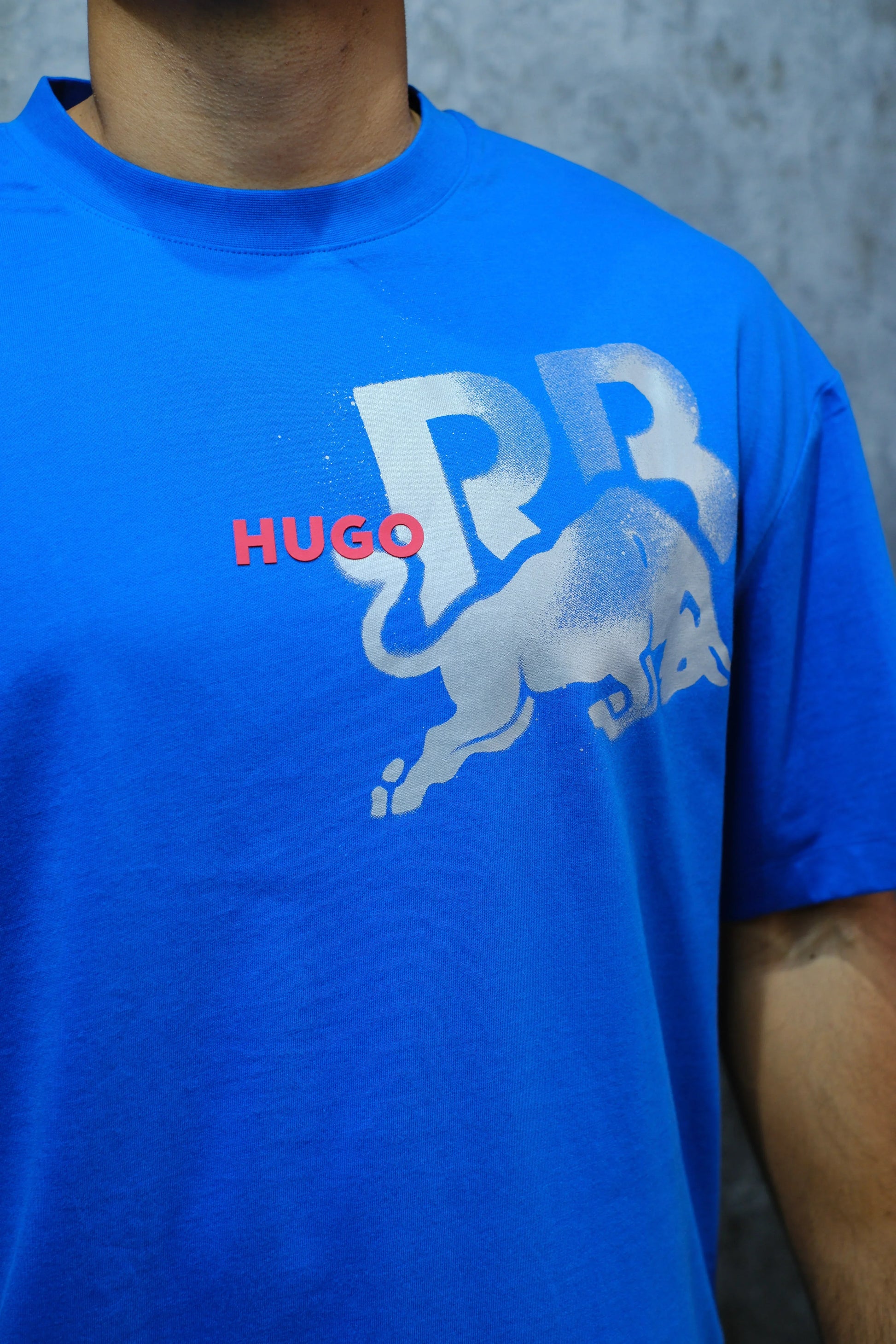 Camiseta azul con estampado de toro y letras "RR", detalle de la palabra HUGO en rojo.